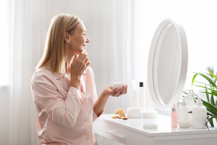 Žena stavlja kremu na lice dok stoji pred ogledalom.