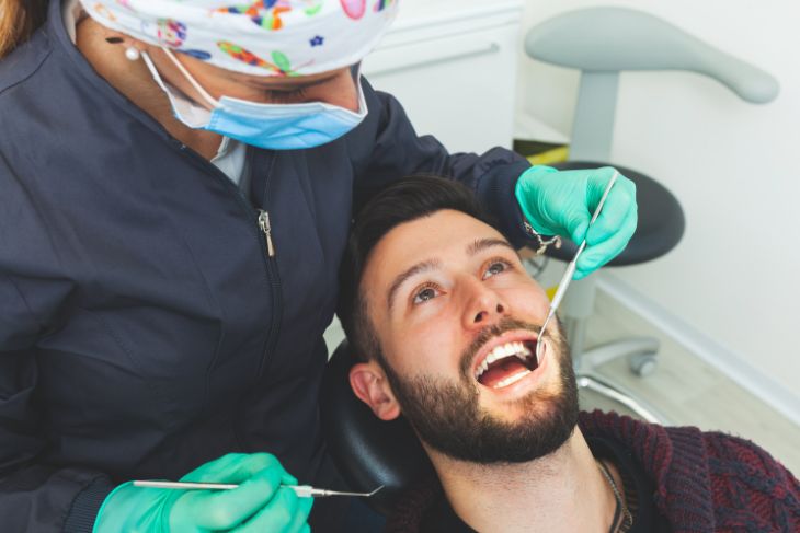 Muškarac u zubarskoj stolici drži usta otvorena dok zubar obavlja pregled.